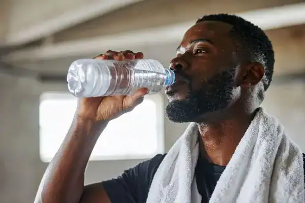 Image of man drinking water to improve hydration Ayr after work out.